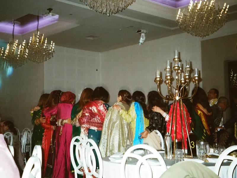 Aunties and cousins in colourful South Asian outfits dancing arm in arm at a wedding banquet hall