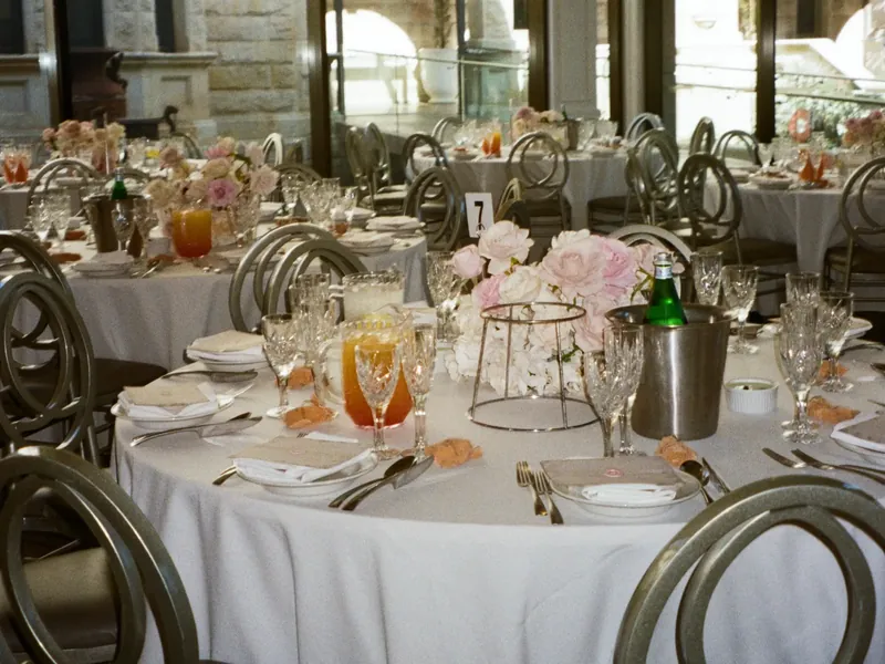 Wedding reception room with round tables, pink and white florals and sunlit windows before guests arrive